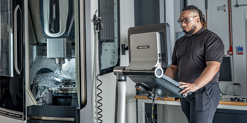 An engineer stands in a work cell and works on a computer